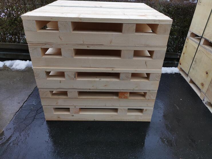 Stapelhaufen aus unbehandelten Holzpaletten auf einem nassen Untergrund, im Hintergrund schneebedeckter Boden.