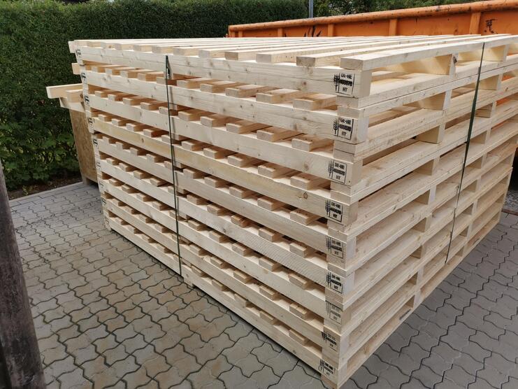 Stapelhaufen aus unbenutzten Holzpaletten auf einem gepflasterten Boden.